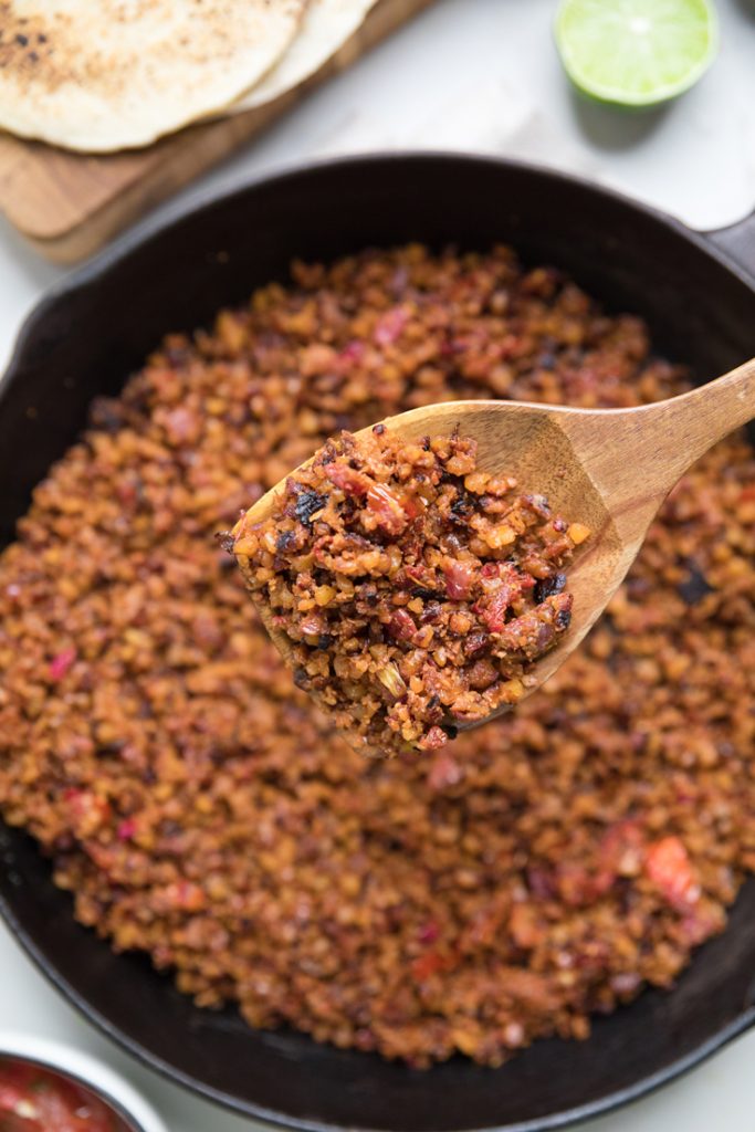 A spoonful of vegan walnut taco meat over a skillet with more meat.