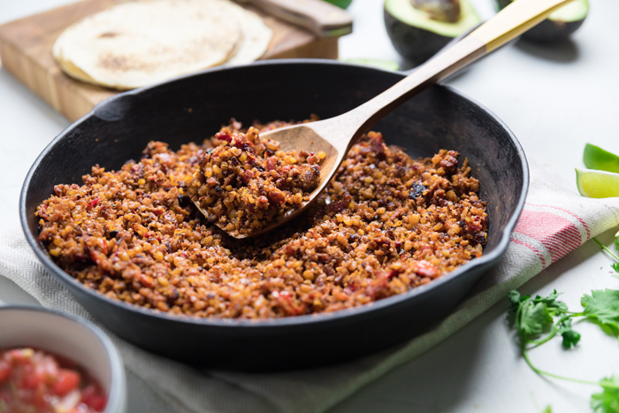 Vegan walnut taco meat on a spoon resting over a skillet.