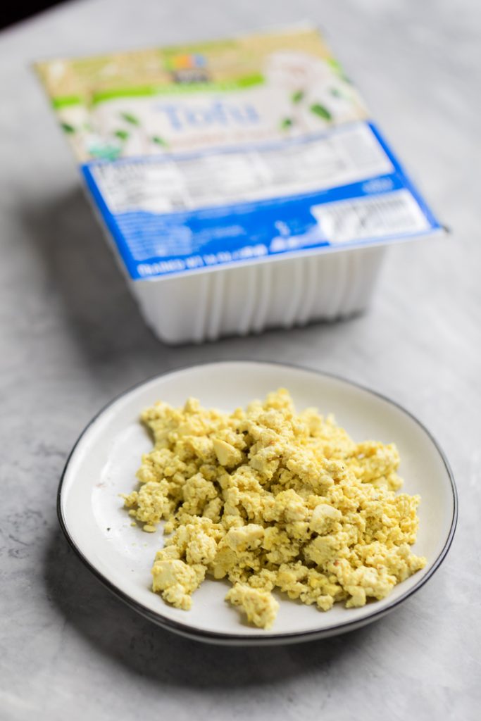 a plate of vegan eggs with tofu package behind it.