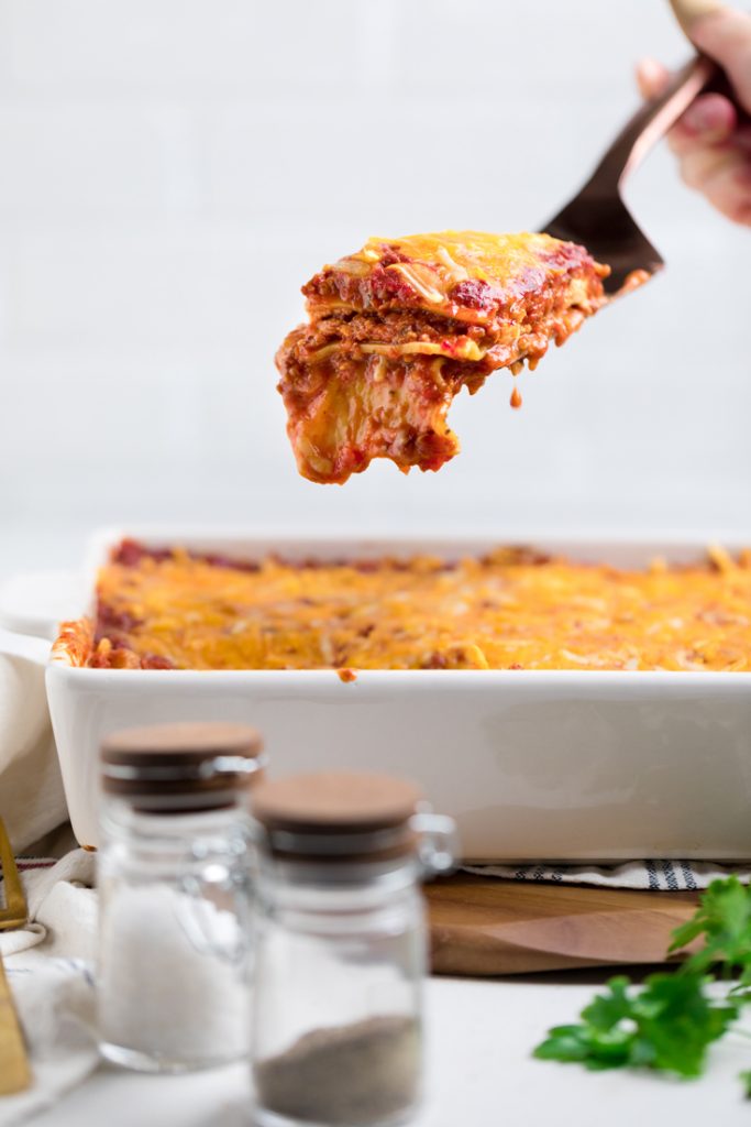 a slice of vegan lasagna on a spatula over a casserole dish .