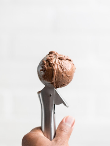 a hand holding an ice cream scooper filled with vegan chocolate ice cream.