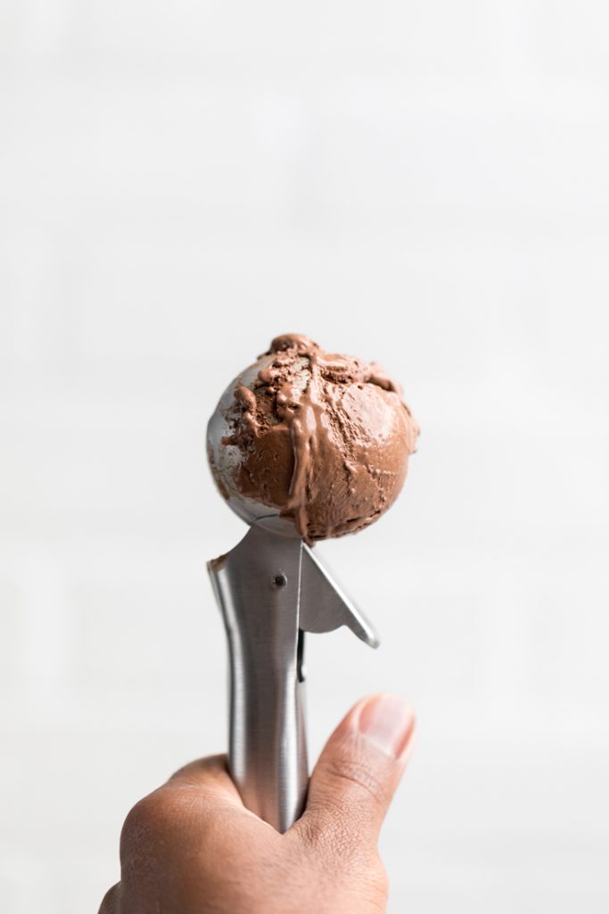 a hand holding an ice cream scooper filled with vegan chocolate ice cream.