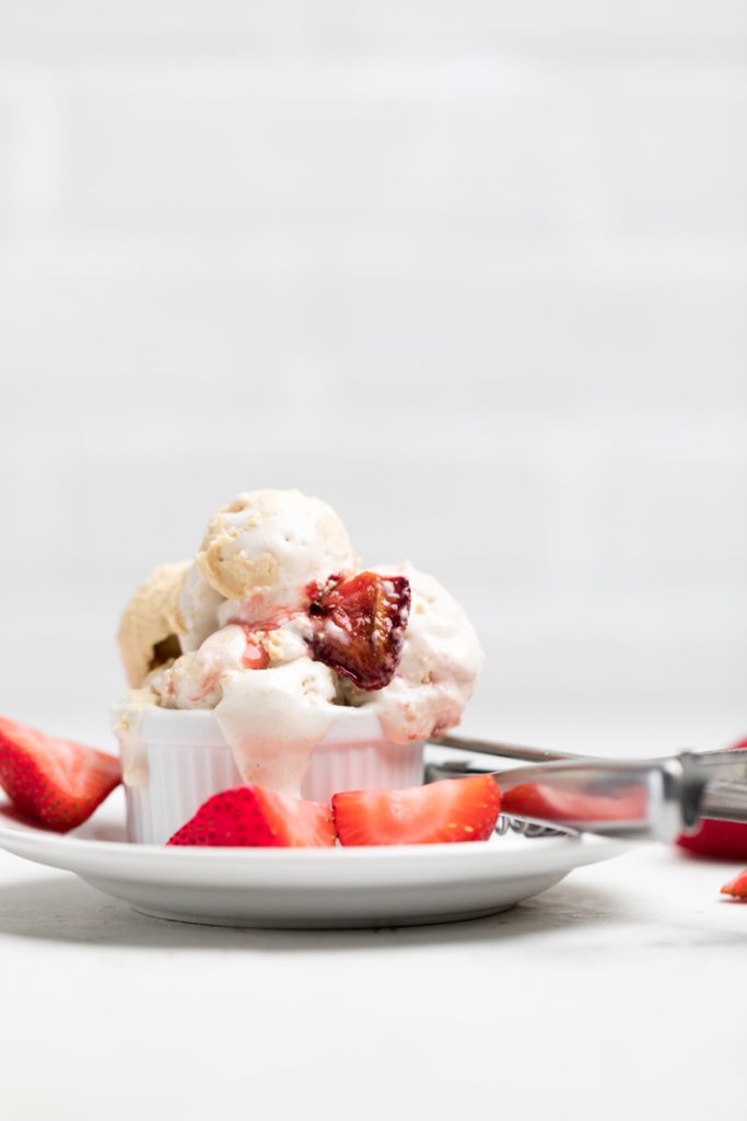 a bowl of vegan peanut butter and jelly ice cream on a plate with fresh strawberries.