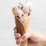 a hand holding a cone of vegan vanilla blueberry peach ice cream.