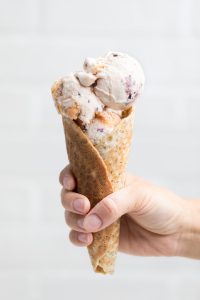 a hand holding a cone of vegan vanilla blueberry peach ice cream.