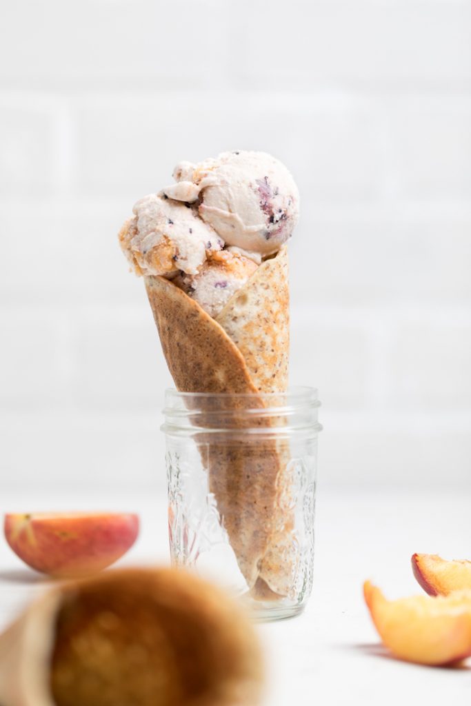 vegan vanilla blueberry peach ice cream in an ice cream cone resting in a jar.