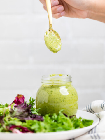 a spoon holding vegan avocado dressing over a jar of the same.