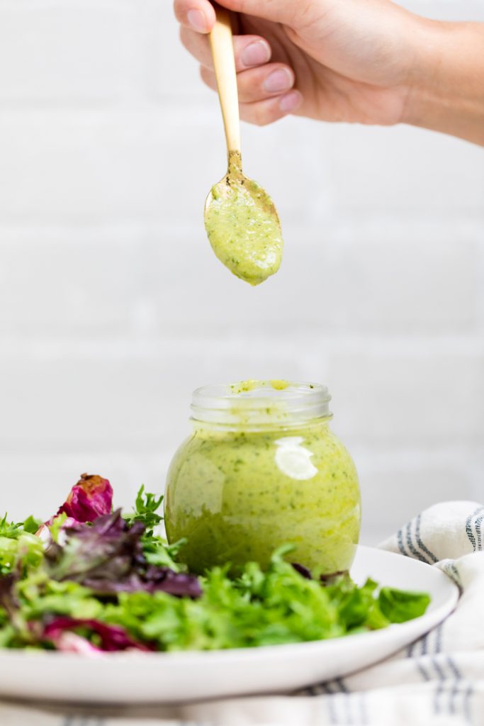 a jar of vegan avocado dressing with a spoon above.