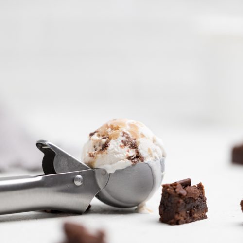 an ice cream scoop filled with vegan salted caramel brownie ice cream and a brownie piece.