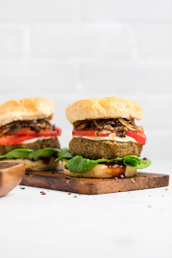 two vegan lentil burgers on a board with fresh toppings.