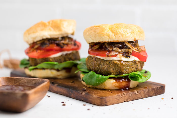two lentil burgers on a wooden board on a white table.