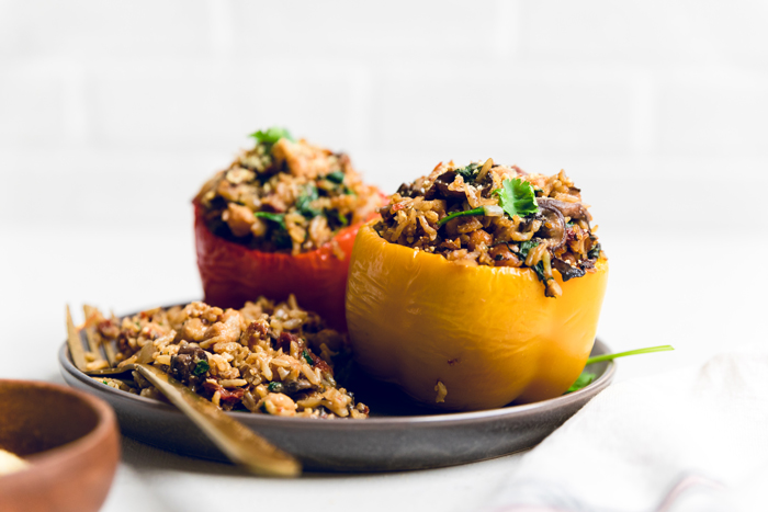a plate with two Tuscan style vegan stuffed peppers and extra filling on the side.