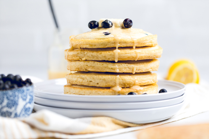 stack of vegan lemon blueberry pancakes with fresh lemon glaze drizzled down side.