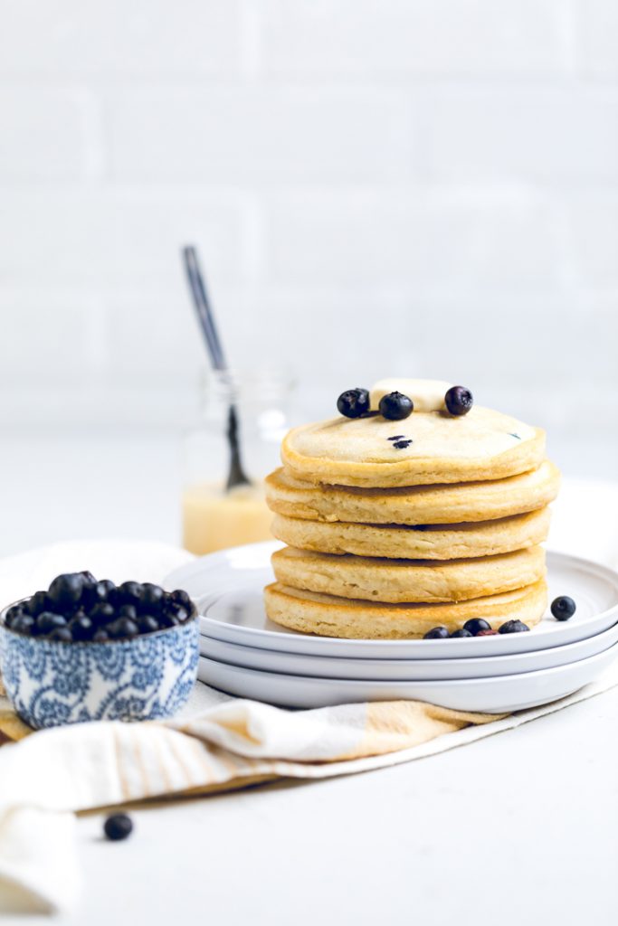 A stack of vegan lemon blueberry pancakes topped with fresh blueberries.