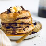 a stack of fluffy vegan chocolate chip pancakes topped with butter and chocolate.