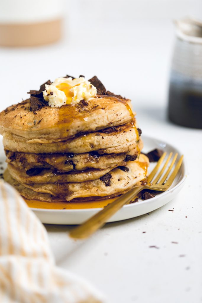 a white plate with a stack of fluffy vegan chocolate chip pancakes.