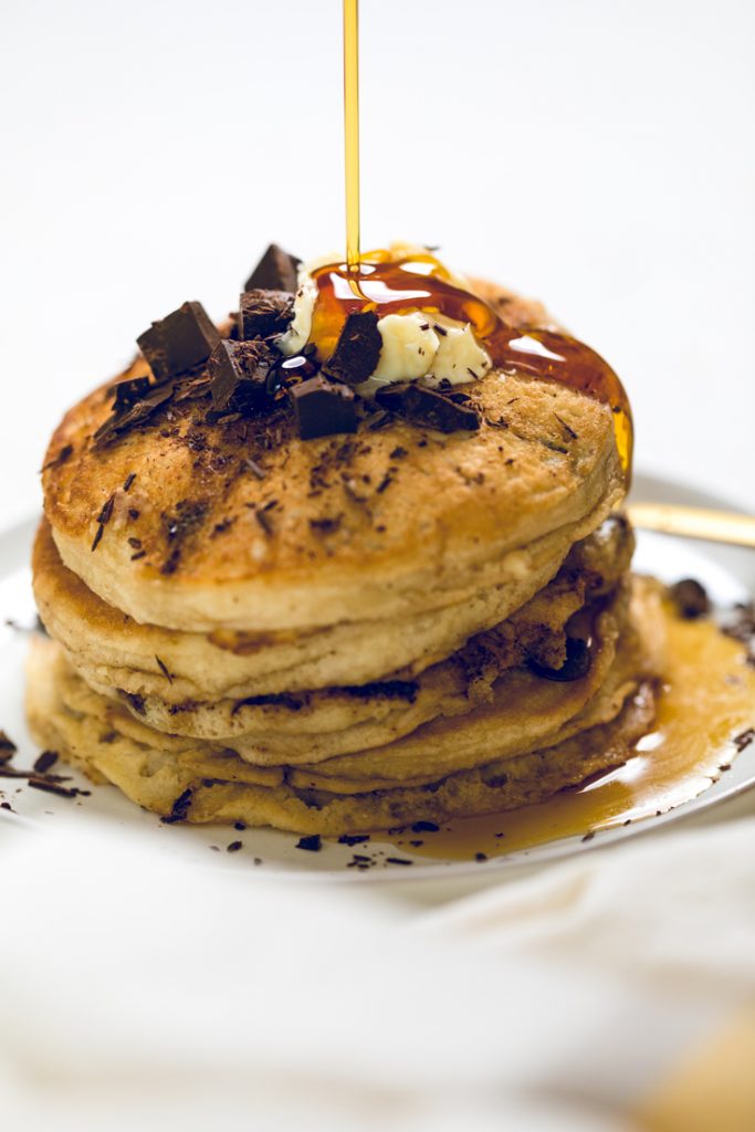 syrup drizzling over a stack of fluffy vegan chocolate chip pancakes.