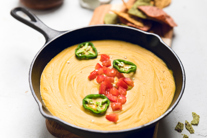 creamy Vegan nacho cheese in a skillet topped with diced tomatoes and jalapeno slices.