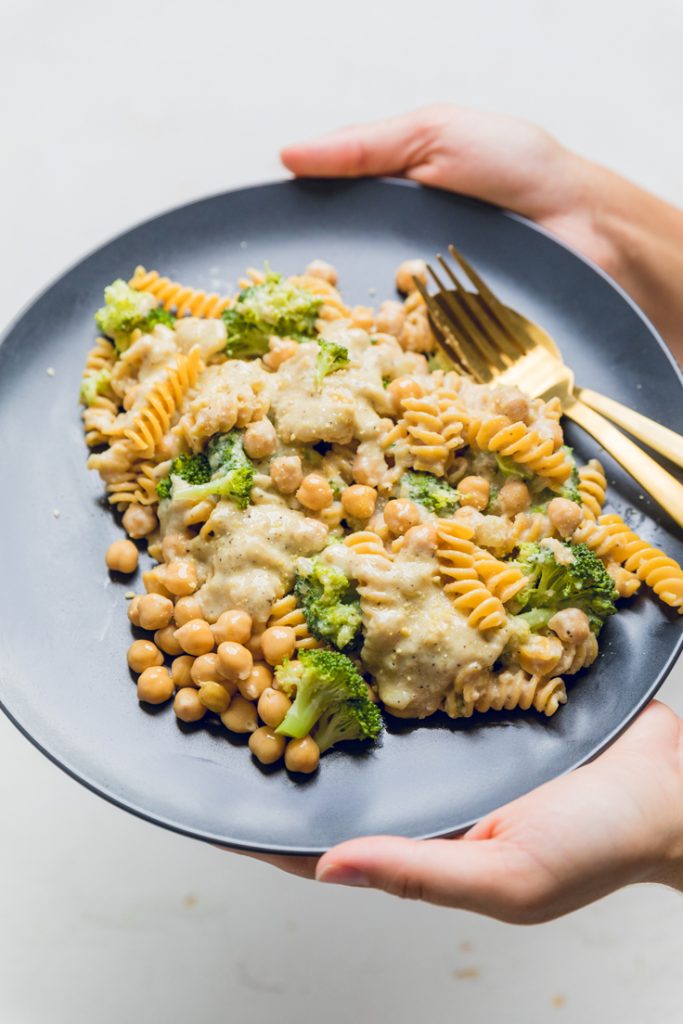 hands holding a plate of vegan creamy broccoli and chickpea pasta.