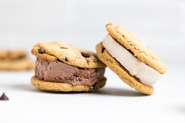 two vegan ice cream sandwiches on a table, one chocolate and one vanilla filled.