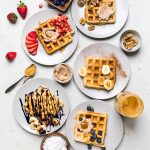 Five plates of easy vegan waffles with an assortment of toppings.