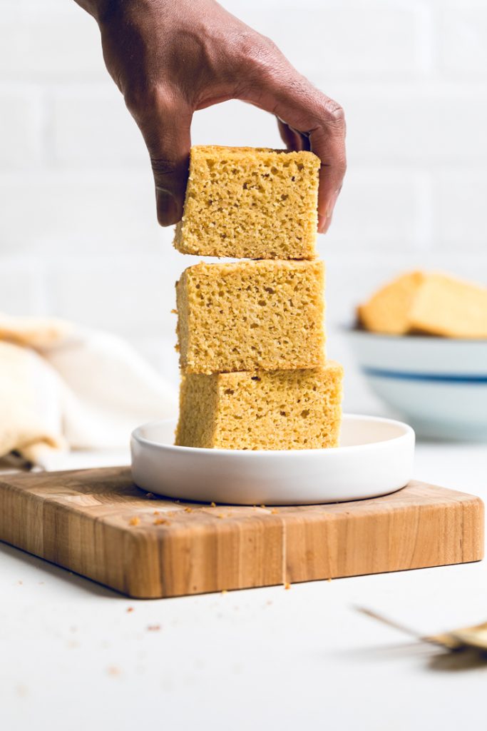 A hand stacking vegan corn bread on a white plate. 