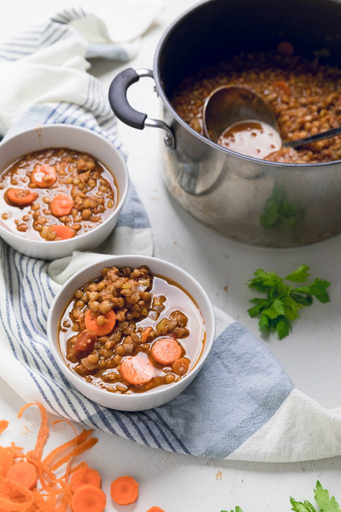 Vegan Lentil Soup in two white bowls with a pot of soup on the side.
