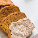 Slices of Vegan pumpkin bread with one piece covered in cinnamon nut butter.