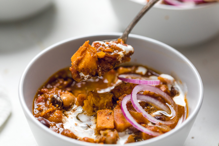 a spoon holding vegan sweet potato chili over a bowl.