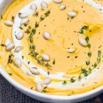 A bowl of vegan butternut squash soup topped with fresh thyme, pepitas, and coconut cream.