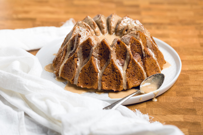 Vegan Pumpkin Bundt Cake with drizzled glaze and a spoon on the side.