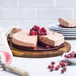 No bake vegan chocolate cheesecake topped with candied cranberries on a wooden board.