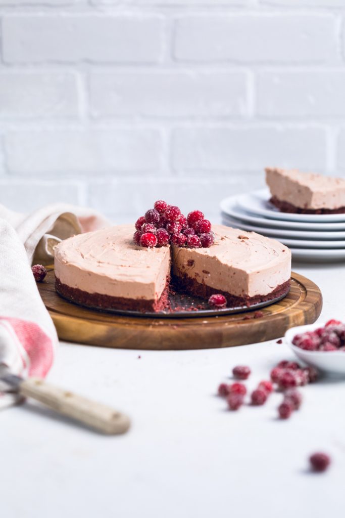 No bake vegan chocolate cheesecake topped with candied cranberries on a wooden board.