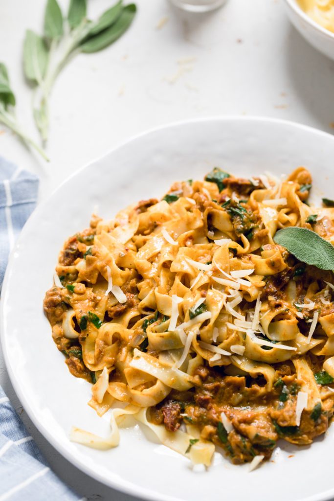A serving of pumpkin pasta with spinach and sundried tomatoes.