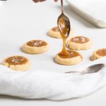 A spoon drizzling caramel into vegan salted caramel cookies.