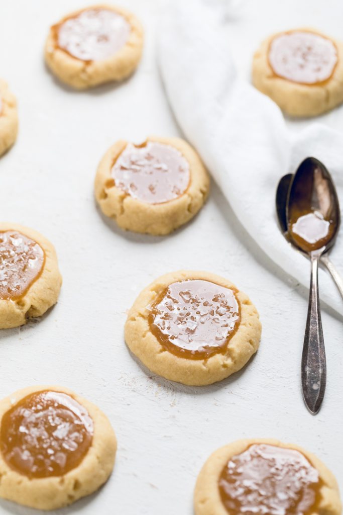 Vegan salted caramel cookies on a white table with a silver spoon of caramel on side. 
