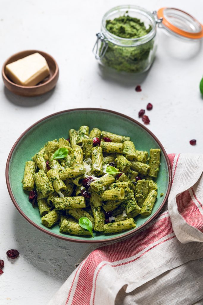 A bowl of vegan pesto pasta with cranberries on a table.