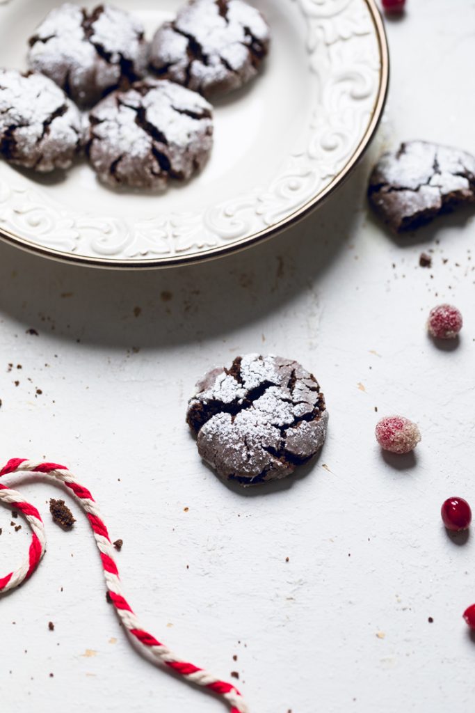 a vegan chocolate crinkle cookie on a table next to a bowl of a batch of them.