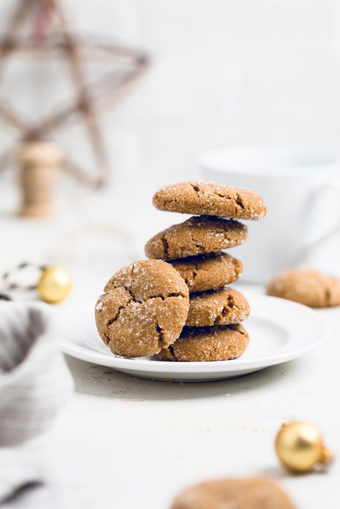 five vegan molasses cookies stacked on a plate with one leaning on the side. 