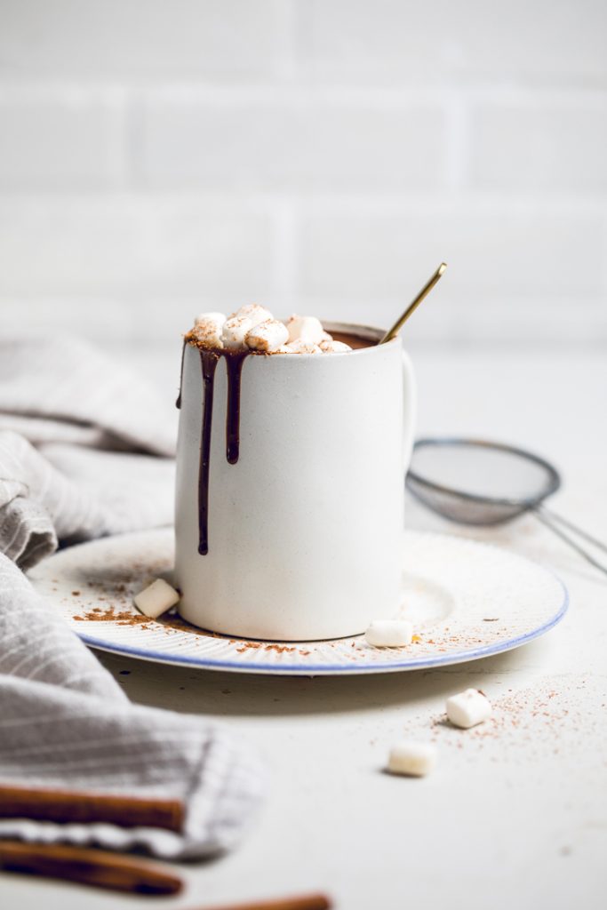 A mug of vegan coconut milk hot chocolate resting on a plate.