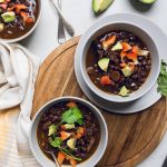 two bowls of vegan black bean soup on a board.