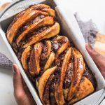 Hands holding a pan with a loaf of chocolate vegan babka.