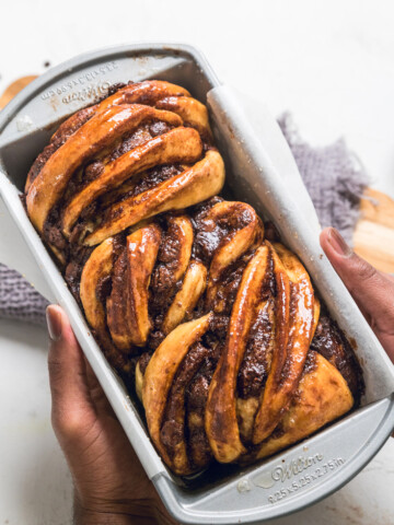 Hands holding a pan with a loaf of chocolate vegan babka.