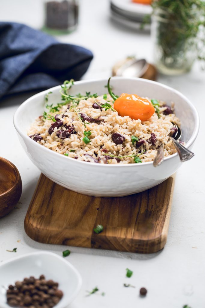 A white bowl of Jamaican rice and peas sitting on a wooden board.