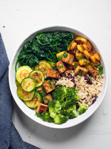 Jamaican jerk tofu rice bowls with broccoli spinach and zucchini slices.