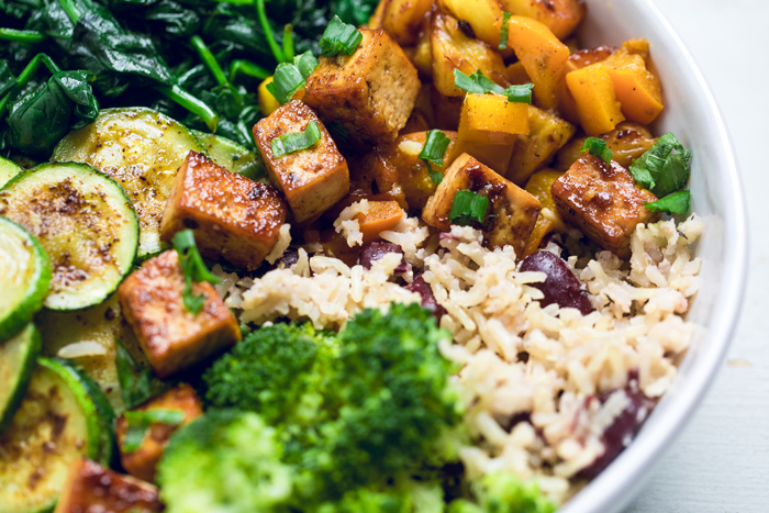 A bowl of Jamaican jerk tofu with rice and peas, cooked mango and broccoli.