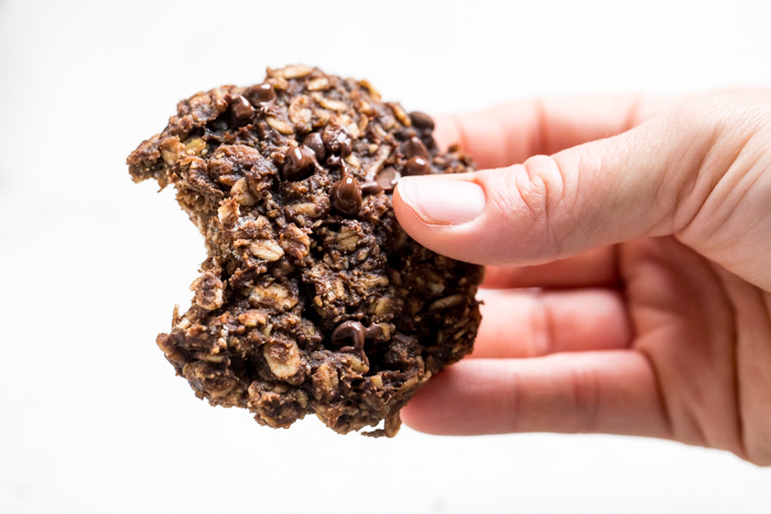 A hand holding healthy vegan chocolate peanut butter banana oatmeal cookie with a bite out.