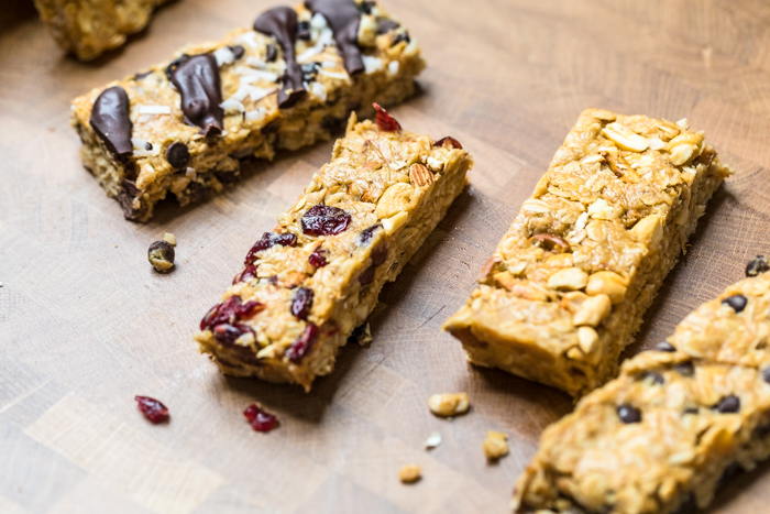 Four homemade vegan granola bars with different toppings on a table.