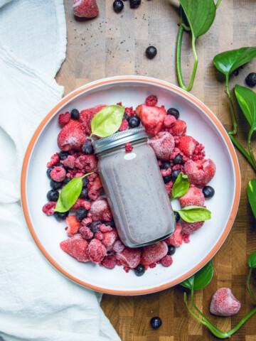 Vegan triple berry smoothie in a jar on top of frozen fruit.