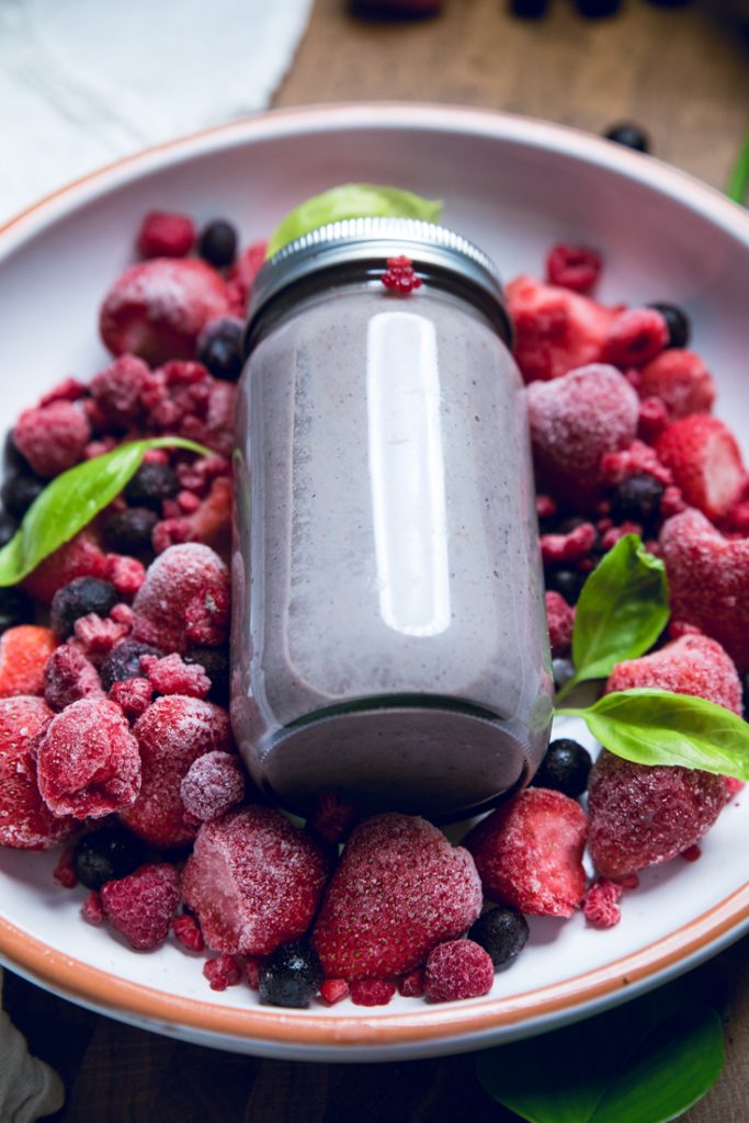 Jar of blended vegan triple berry smoothie over fruit.